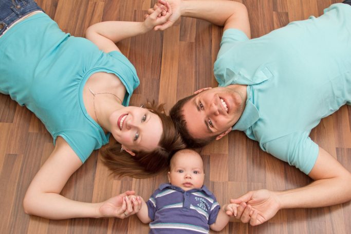 Baufamilie Ein Paar liegt auf dem Boden und hält ihren Baby-Sohn. Alle wirken glücklich.
