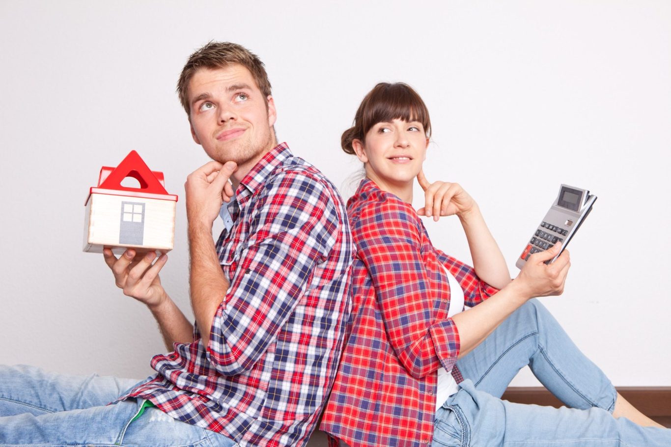 Bauherren Junges Paar sitzt Rücken an Rücken, denkt nach, hält ein Hausmodell und ein Smartphone.