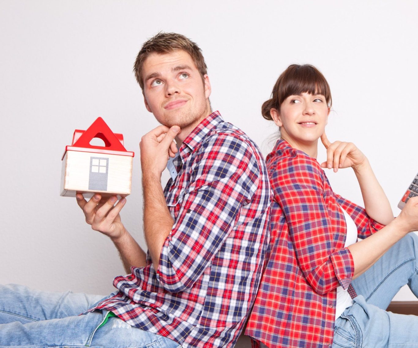 Bauherren Junges Paar sitzt Rücken an Rücken, denkt nach, hält ein Hausmodell und ein Smartphone.