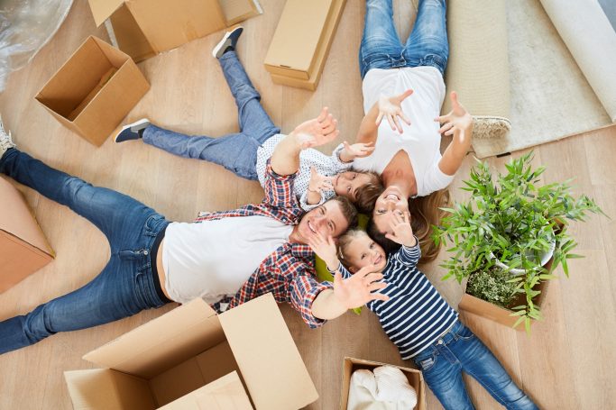 Baufamilie Familie liegt entspannt im Raum, umgeben von Umzugskartons und einer Pflanze.