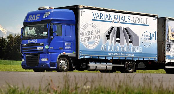 LKW VHG Bausatzhaus Blauer Lkw mit Werbung für einen Möbeltransportdienst auf einer Landstraße.