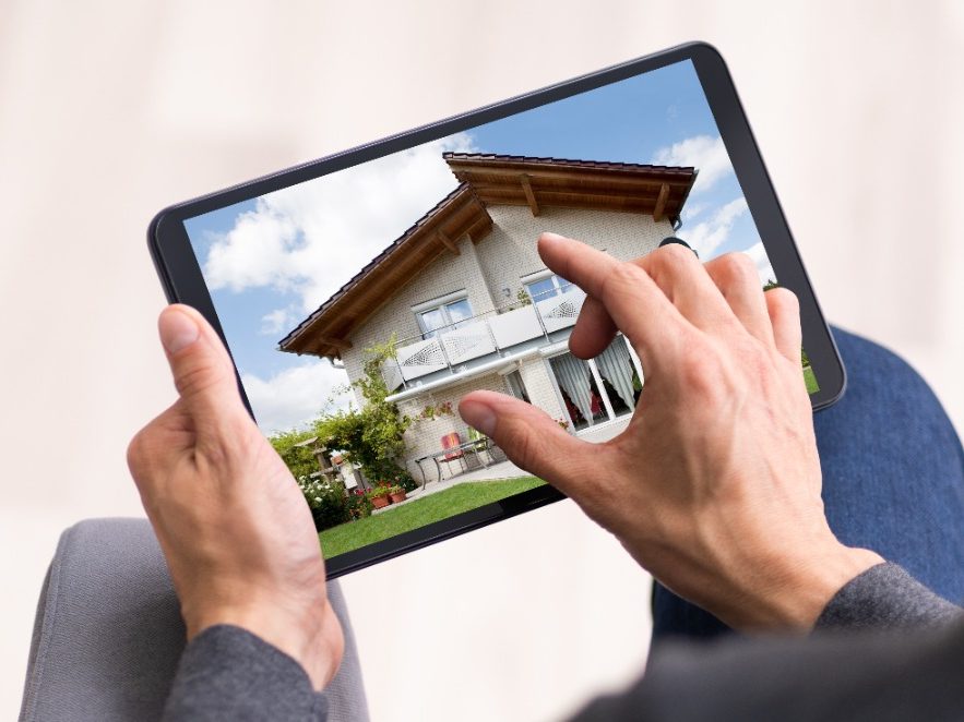 Hausbau - individuelle Planung Eine Person betrachtet ein modernes Haus auf einem Tablet mit einem Garten.