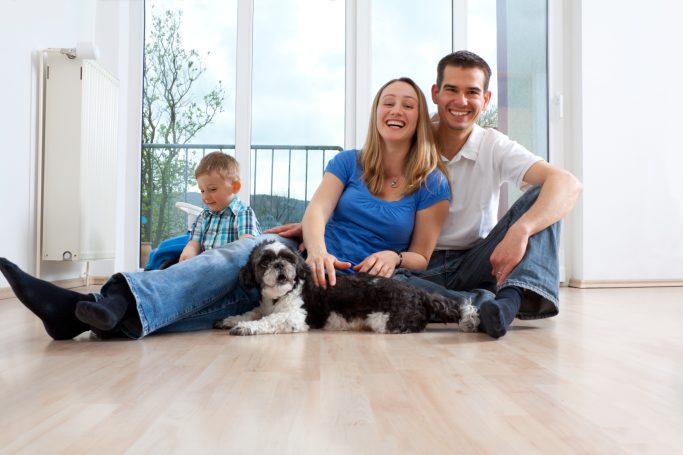 Baufamilie Eine glückliche Familie sitzt auf dem Boden, mit einem Kind und einem kleinen Hund.