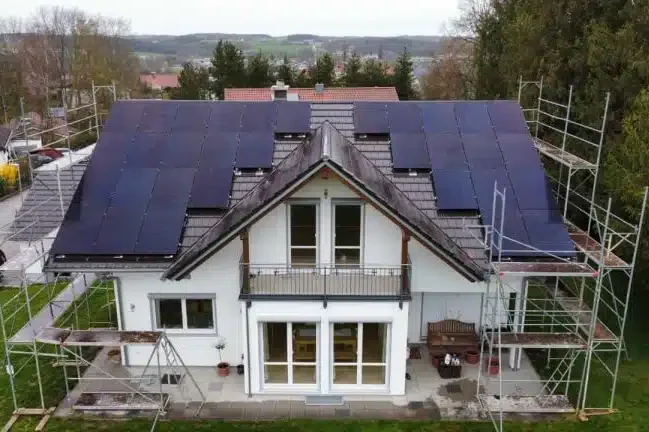 PV Anlage - SolarHelden - Massivhaus / Fertighaus Vertrieb Moderne Villa mit Solarpanels auf dem Dach und Baugerüst rundherum.